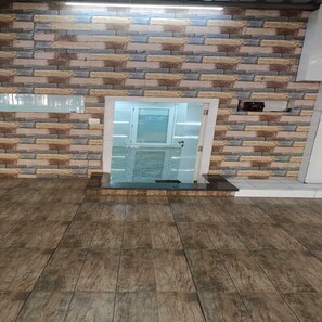 A room with a stone-patterned wall, a glass door leading to a bathroom, and a wooden floor.