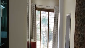 Quarto com uma janela grande, uma cadeira vermelha e uma TV fixada na parede.