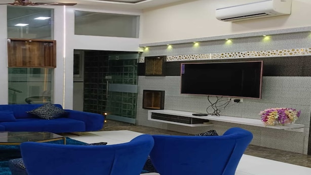 Uma sala de estar moderna com um sofá azul, uma TV de tela plana fixada em uma parede texturizada e um ventilador de teto.