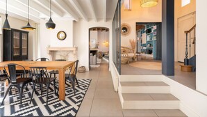 Amplia sala de estar con una mesa de comedor de madera, sillas negras y un tapete estampado. Se ve una escalera que conduce a un nivel inferior con una estantería y una zona de estar acogedora.