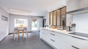 Una cocina moderna con armarios blancos, un ventanal grande y un comedor con mesa y sillas.