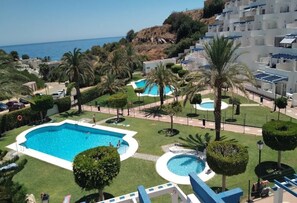 Relax by the resort's central pool, surrounded by lush lawns and palm trees, with a view of the sea.