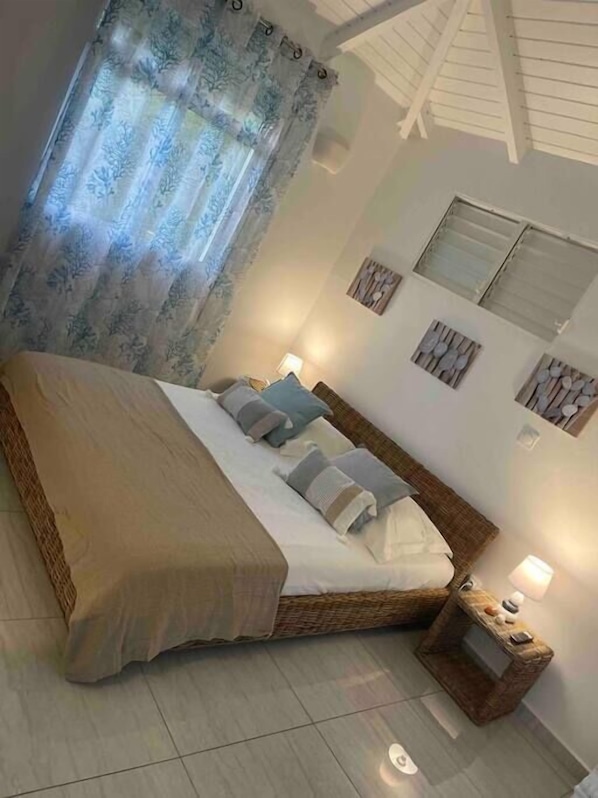 Une chambre à coucher avec un grand lit, une table de chevet et une fenêtre avec des rideaux.