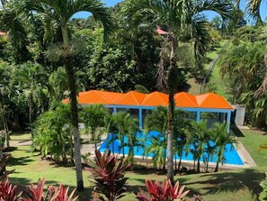 Un complexe hôtelier doté d’une piscine, de palmiers et d’un bâtiment surmonté d’un toit orange.