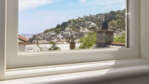 A view through a window of a coastal town with buildings on a hillside, a chimney, and a clear sky. - Mermaid Cottage (Penzance)