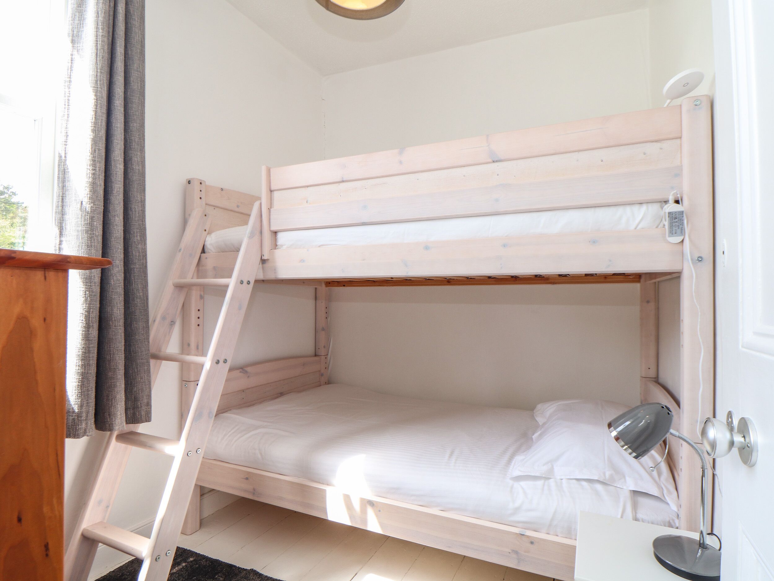 A bunk bed with a ladder, a bedside table, and a desk lamp.