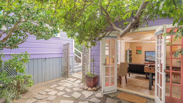 Un patio con pavimento in pietra, un'area salotto con tavolo e sedie e vista su un edificio viola sullo sfondo.