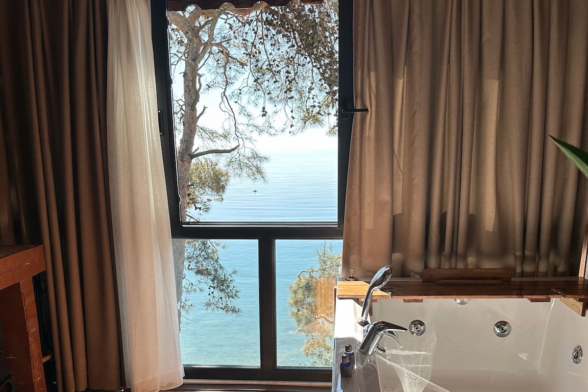 A room with a large window, a bathtub, and a wooden floor.