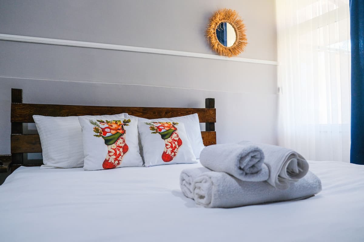 A neatly made bed with white bedding and decorative pillows, a rolled towel, and a mirror on the wall.