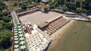 An aerial view of a beachside resort with rows of sun loungers and umbrellas, a swimming pool, and a beach area with lounge chairs. - Yörükali Tesisleri (Adalar)