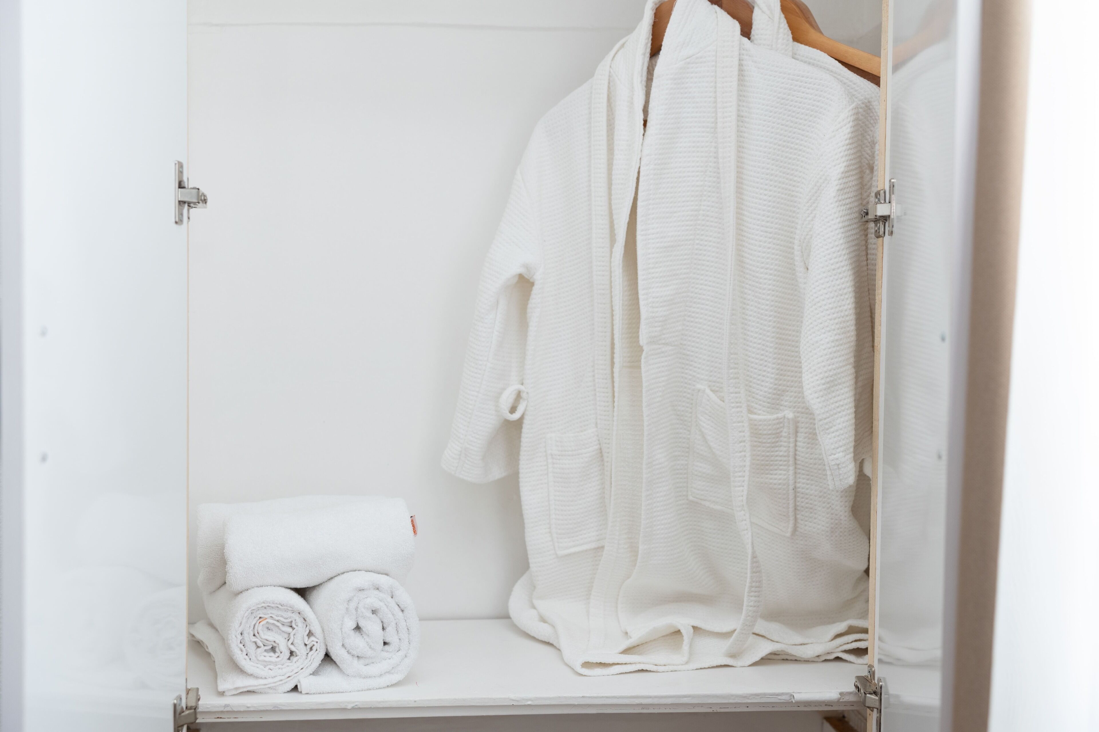 A white wardrobe with a hanging robe and rolled towels.