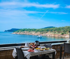 Una mesa dispuesta con comida y bebidas, con vista a un cuerpo de agua y un barco a lo lejos.
