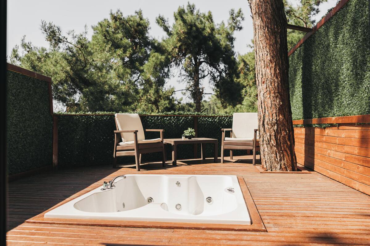 A wooden deck with a hot tub, two chairs, and a small table.