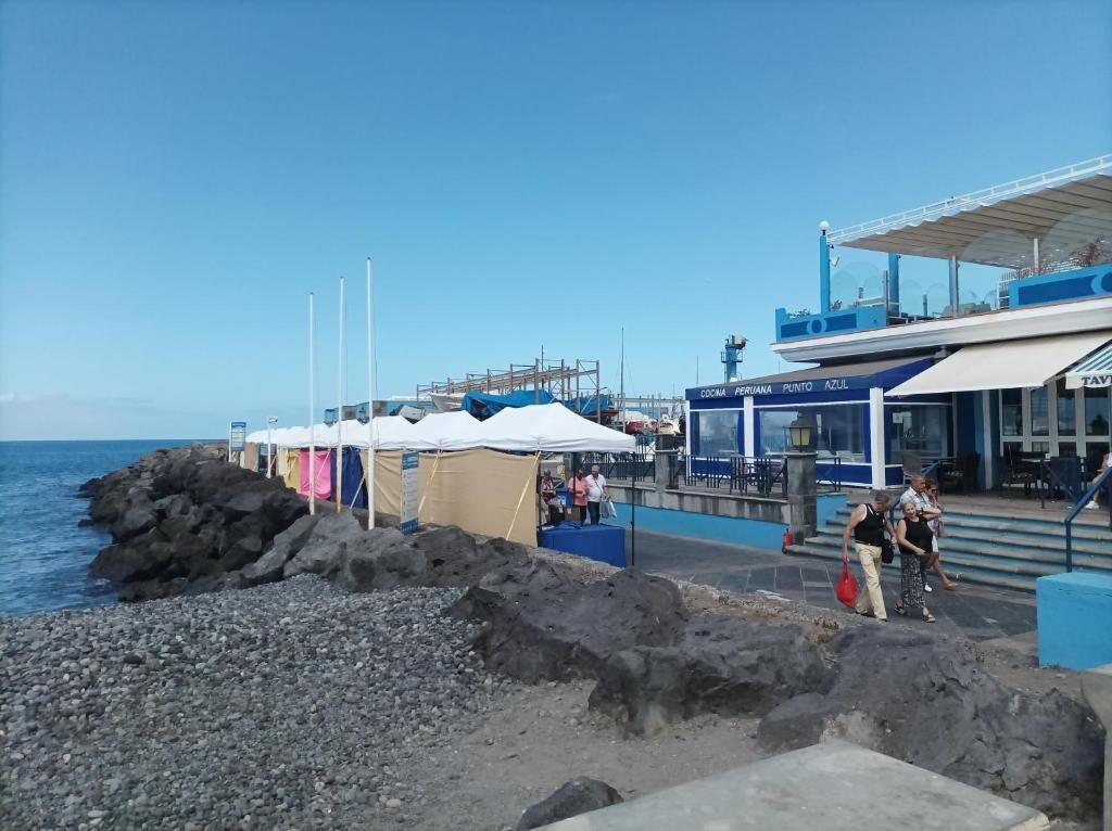 Uma área costeira com um litoral rochoso, um restaurante chamado 'COCA PERUANA PUNTO AZUL' e algumas pessoas passando.