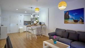 A modern living room with a grey sofa, a coffee table with a potted plant, and a dining area with a white table and chairs. - Apartamento Sol y Mar (Arona)