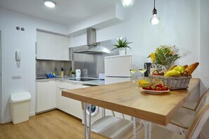 Une cuisine moderne avec des meubles blancs, des appareils en acier inoxydable et une table à manger en bois agrémentée de fruits et de fleurs.