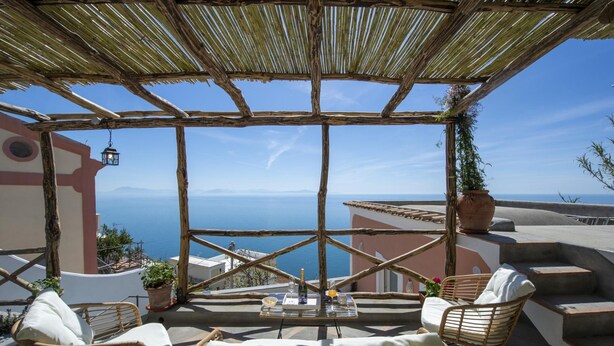 A terrace with wicker furniture, a table with a bottle and glasses, and a view of the sea. - Casa Terry - Lovely Apartment With sea View (Praiano)