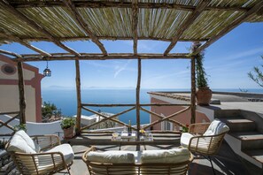 Una terrazza con mobili in vimini, un tavolo con una bottiglia e dei bicchieri, e vista sul mare.