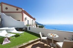 A rooftop terrace with white lounge chairs, a small table with breakfast items, and a view of the sea. - Casa Terry - Lovely Apartment With sea View (Praiano)
