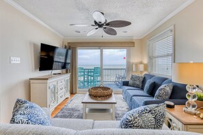 Ein Wohnzimmer mit Fernseher, Deckenventilator, einer Couch, einem Couchtisch und Meerblick vom Balkon.