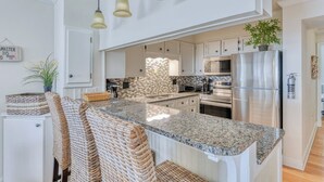 A modern kitchen with a granite countertop, stainless steel appliances, and a hanging light fixture. - Sea Master 315 - Three Bedroom, Three Bathroom, Oceanfront Condo (Garden City Beach)
