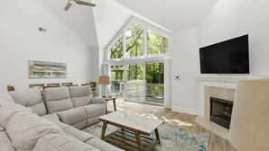 Un salon spacieux comprenant un grand canapé d’angle, une cheminée, un téléviseur et un balcon doté de grandes fenêtres.