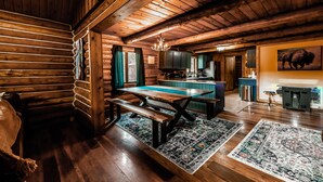 Ein rustikales Blockhaus-Interieur mit einem Holzespeisesaal, Bänken, einer Chandelüster und einer Küchenzeile.
