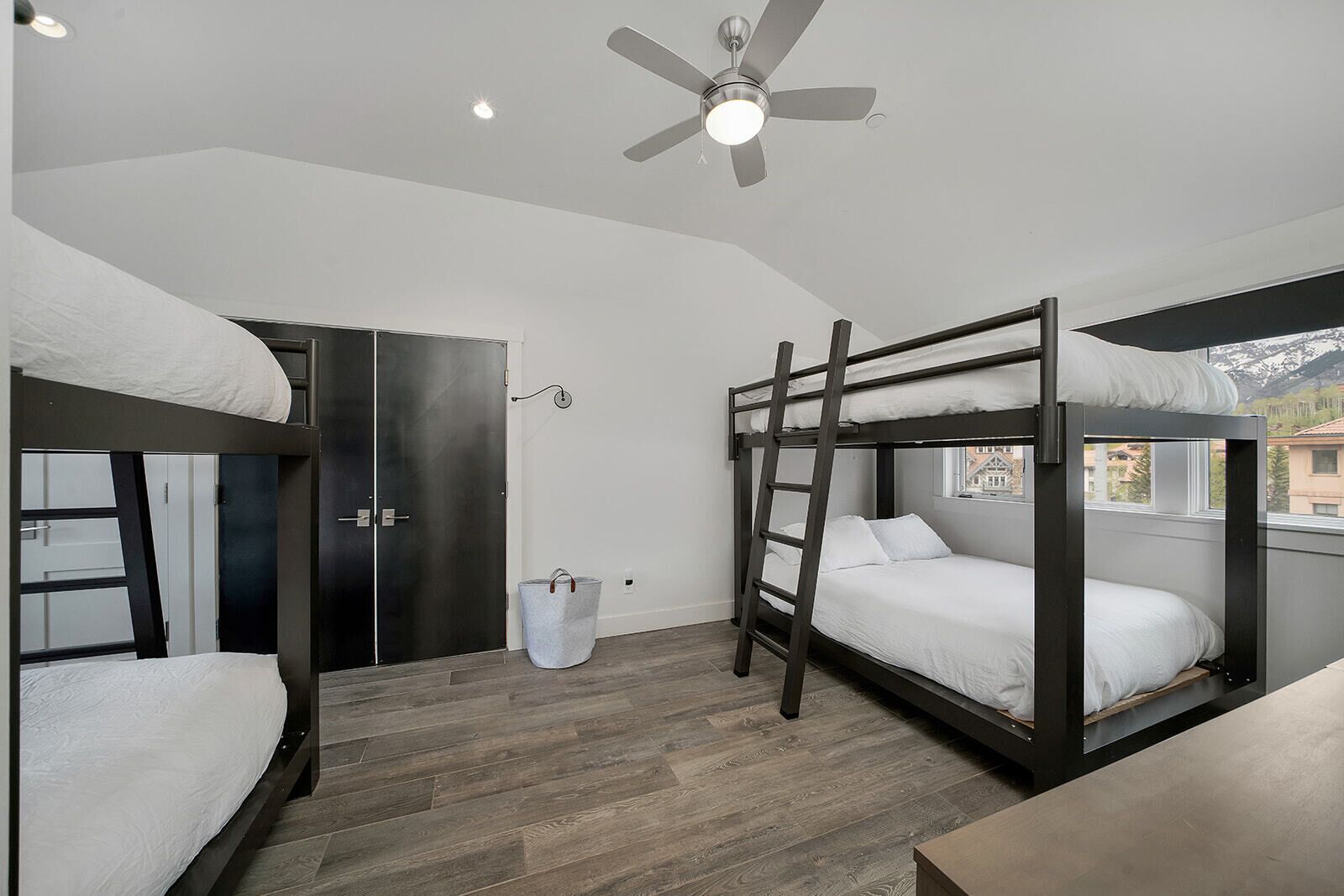 Une chambre avec un lit superposé, un ventilateur de plafond, une fenêtre avec vue et une porte en métal.