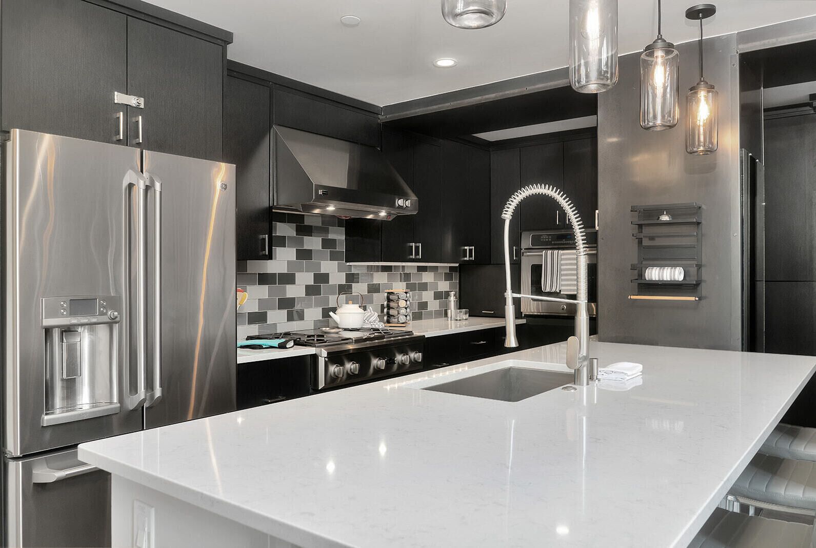 A modern kitchen with stainless steel appliances, a white countertop, and a black backsplash.