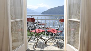 Een balkon met rode stoelen en een tafel, met uitzicht op een meer met boten en bergen op de achtergrond.