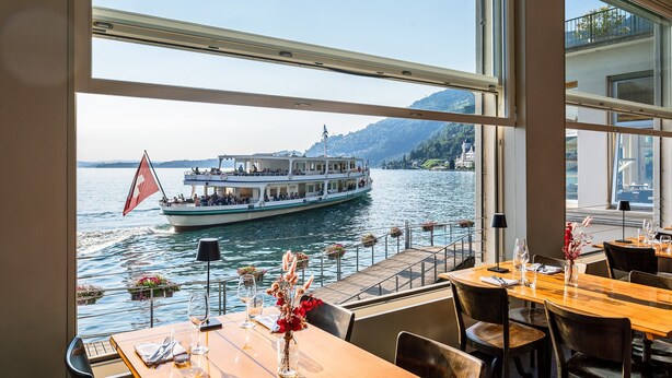 Een restaurant met uitzicht op een meer en een boot. Tafels zijn gedekt met wijn en bloemen.