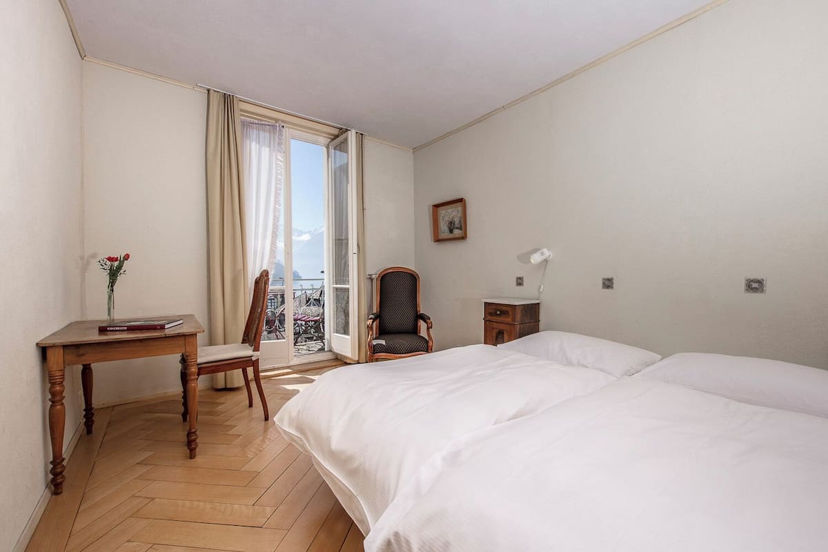Ett hotellrum med en säng, ett skrivbord, en stol, ett litet bord och ett fönster med utsikt över cyklar och ett berg.
