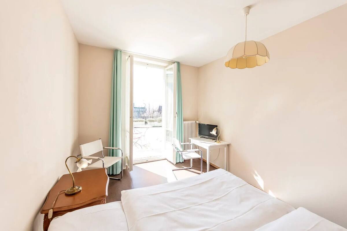 Ett hotellrum med en säng, ett skrivbord, en stol, en lampa och utsikt över omgivningarna.