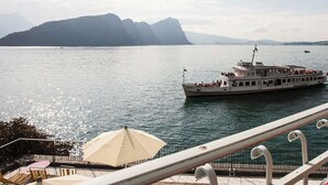 Een veerboot met passagiers, een dek met tafels en stoelen, en een bergachtig landschap op de achtergrond.