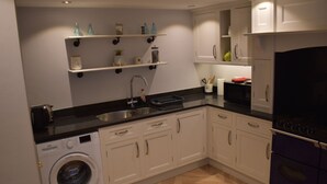 A compact kitchen with white cabinets, a washing machine, a sink, and a stove.