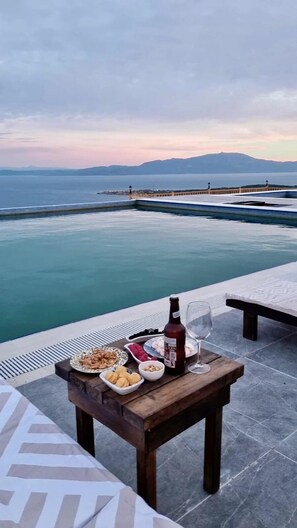 A table with food and drinks on a terrace overlooking a body of water and mountains. - Assos Karadut Taş Otel (Ayvacik)