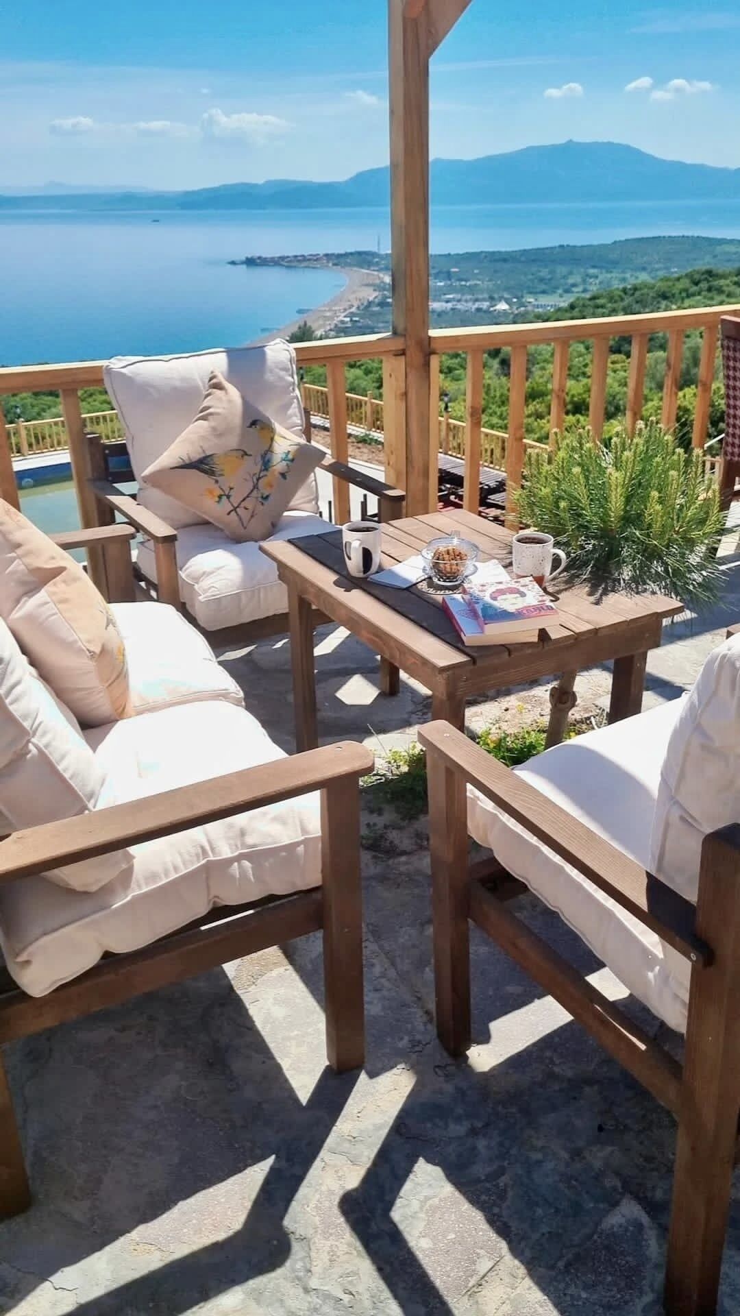 Una terraza de madera con mobiliario exterior, una mesa con un tazón de nueces, una taza y un libro.