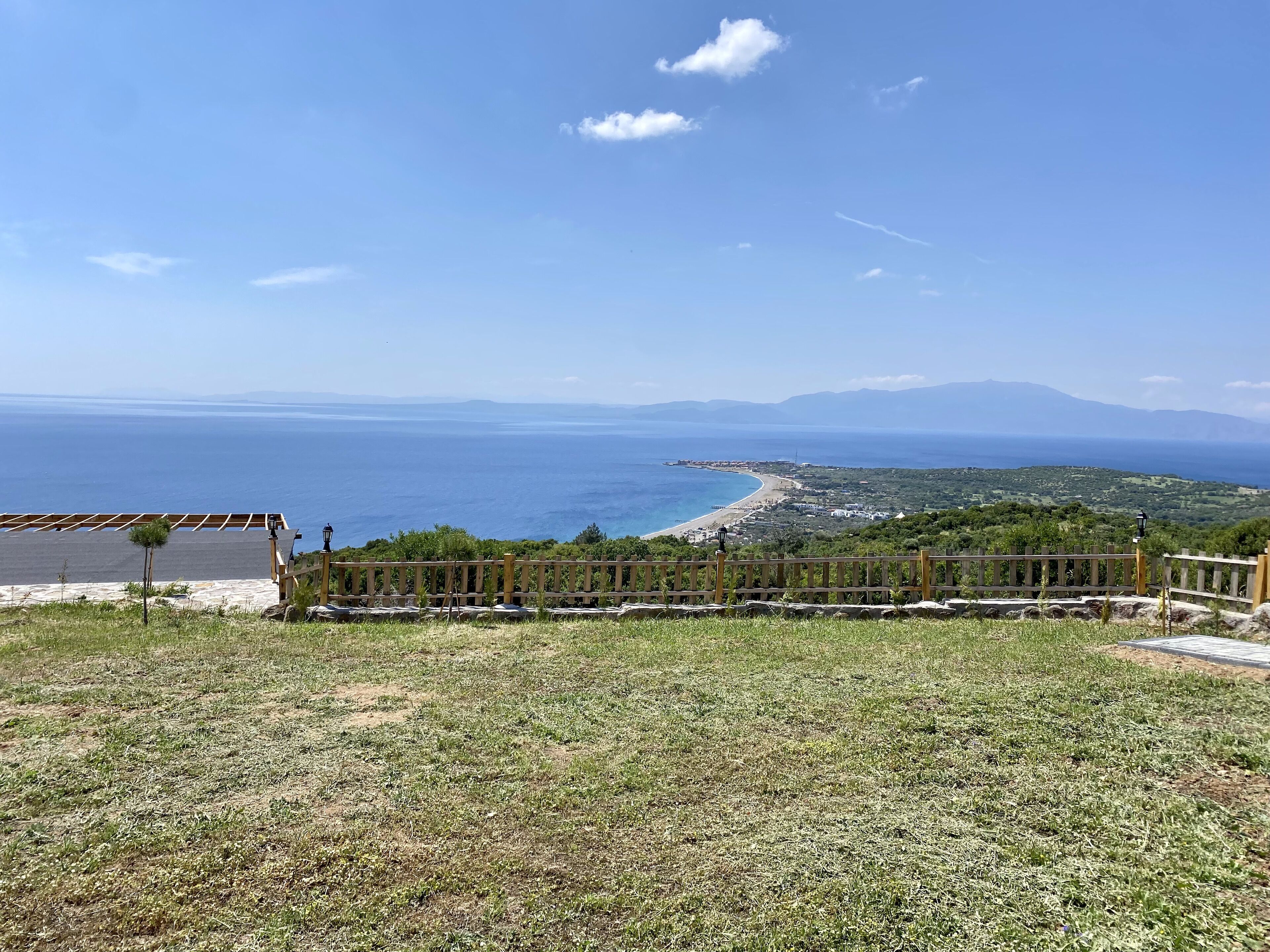 A coastal view with a wooden fence, a paved area, and a distant beach.