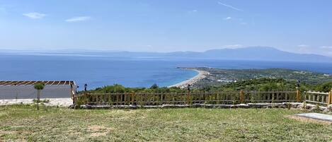 A coastal view with a wooden fence, a paved area, and a distant beach.