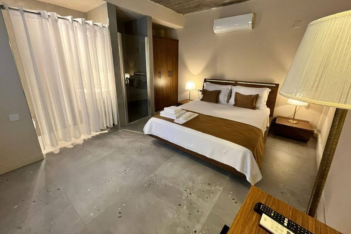 Habitación de hotel con cama, mesita de noche, lámpara y un control remoto sobre la mesa.
