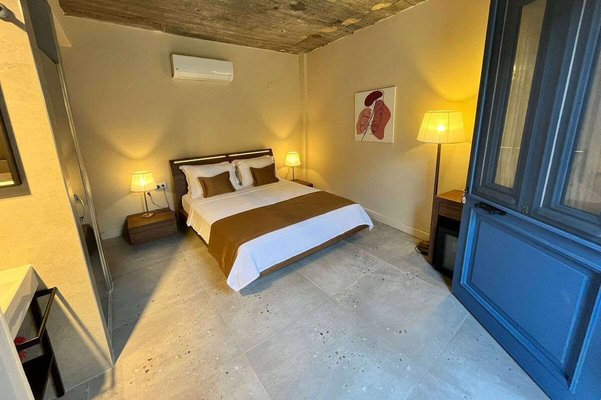 Un dormitorio con una cama, lámparas de noche, aire acondicionado de pared y una puerta.