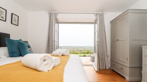 A bedroom with a large bed, a wardrobe, and a view of the countryside. - Trevilges Cottage (Helston)