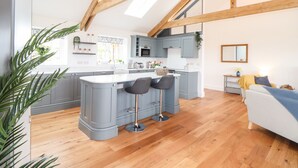A modern kitchen with a central island, bar stools, and a dining area with a sofa. - Trevilges Cottage (Helston)