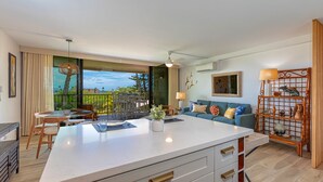 A modern kitchen with a large island, dining area with chairs, a sofa, and a decorative shelf.