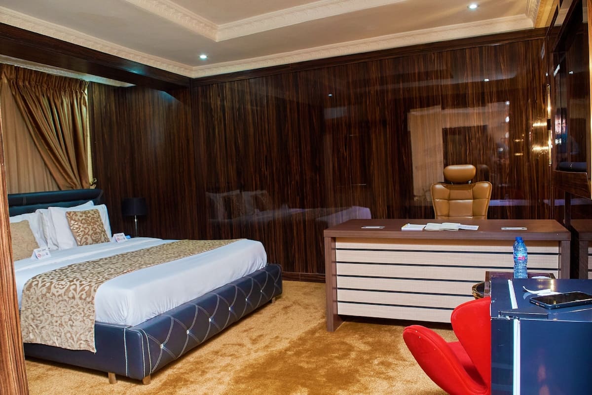 Quarto de hotel com cama, escrivaninha, cadeira e poltrona vermelha.