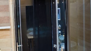 A modern elevator with a metallic finish and a glass door, located in a room with wooden paneling and a visible toilet. - No.1 Hotel Ibadan (Ibadan)