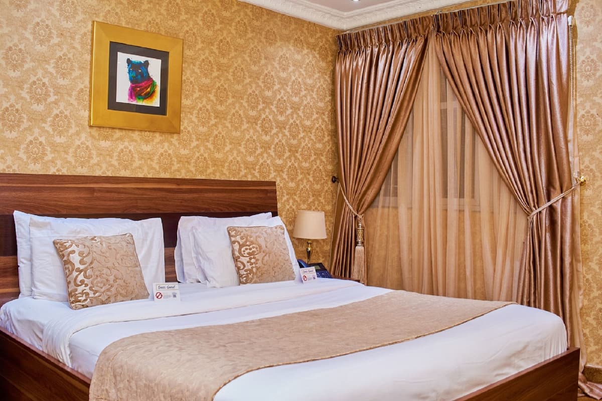 Cama bem arrumada com lençóis brancos e manta marrom, cabeceira de madeira e quadro na parede.