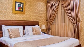 A neatly made bed with white linens and a brown throw blanket, a wooden headboard, and a framed picture on the wall.
