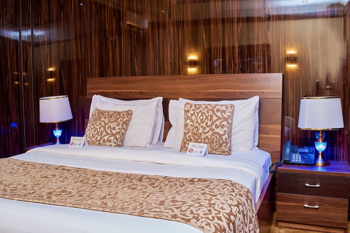 Quarto de hotel com uma cama grande, duas luminárias de cabeceira, uma mesinha de cabeceira com telefone e um aviso de 'Não Perturbe'.