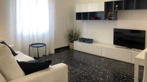 A modern living room with a white sofa, a black-framed TV, and a black and white speckled floor.